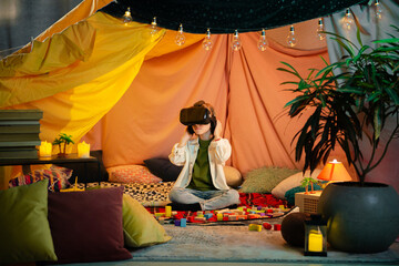 Obraz na płótnie Canvas The boy are hanging out in a children s blanket tent indoors while playing with a vr headset and enjoying their time laughing together