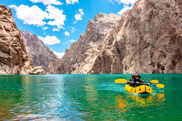 Kayaking on a mountain lake. Two men are sailing on a yellow canoe along the lake along the rocks....