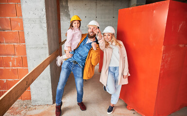 Fototapeta na wymiar Man holding daughter and smiling. Happy couple real estate house buyers demonstrating keys from new home under construction. Family life and new home purchase concept.
