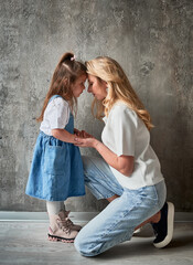 Side view of cute child with mother standing against the wall at home. Blonde woman holding daughter hand. Family and motherhood concept.