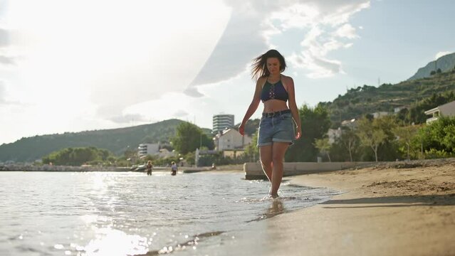 The girl is walking along the ocean shore, splashing the water with her feet. A Caucasian woman walks along the seashore. slow motion video. High quality 4k footage