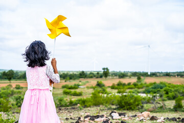 Back view shot of girl kid playing cardboard paper fan at wind turbine - concept of freedom, childhood lifestyle and development.