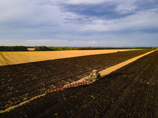 Tractor with harrow system plowing ground on cultivated farm field