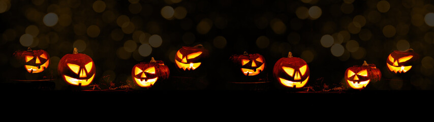 Scary Halloween celebration holiday background banner panorama - Many spooky carved pumpkins on dark night sky with bokeh lights