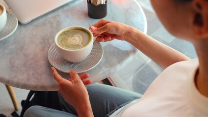 Top view of a girl taking a sip of matcha green tea latte a latte art on it. Healthy food and drinks