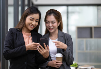 Two asian businesswoman in formal suit in office happy and cheerful during using smartphone and working in the office.