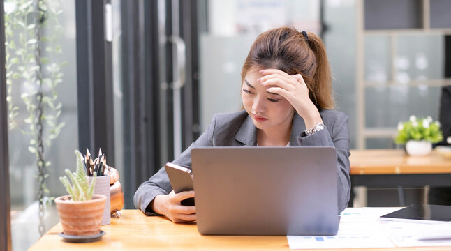 Serious Young Asian Businesswoman At Her Office Desk Dealing With A Smartphone Problem Or Receiving A Complaint Email From Her Boss.