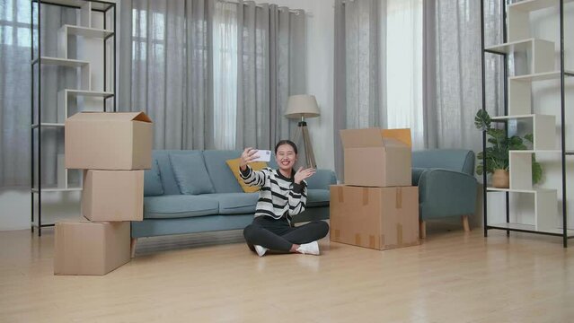 Young Asian Woman With Cardboard Boxes Sitting On The Floor And Taking Photo By Smartphone After Moving Into A New House 
