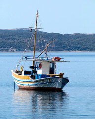 A traditional Greek fishing boat "kaiki" lays in the calm sea under a clear blue sky.