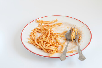 Leftover pasta on plate with cutlery over white background.