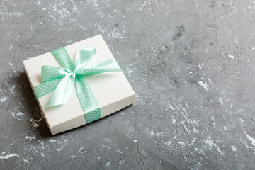 wrapped Christmas or other holiday handmade present in white paper with green ribbon on colored background. Present box, decoration of gift on colored table, top view with copy space