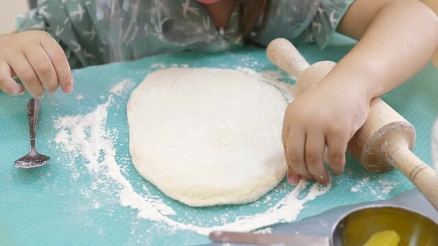 Closeup 5-year old girl rolls out raw dough with a small rolling pin on a silicone mat. Preparing dough for baking pizza, pie. Making a thin baking dish.Stages of baking and confectionery preparation.