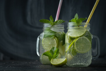 Refreshment mojito cocktail with mint and lime in a glass mug on a black background. Cold summer drink with ice