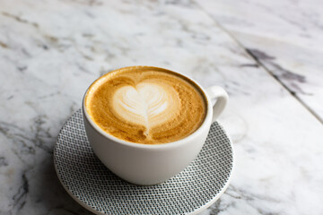 Trendy pink cup of hot cappuccino on marble table background. Heart shape latte art for symbol of love.