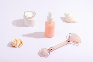 Obraz na płótnie Canvas Facial roller, cosmetic serum bottle and cream jar on white background with seashells. Beauty, spa and selfcare concept. Top view