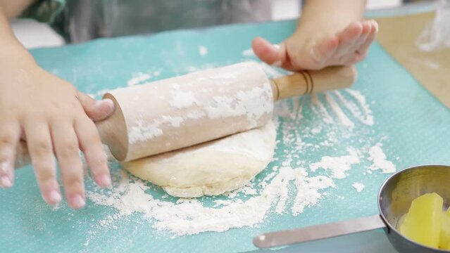 Closeup 5-year old girl rolls out raw dough with a small rolling pin on a silicone mat. Preparing dough for baking pizza, pie. Making a thin baking dish.Stages of baking and confectionery preparation.