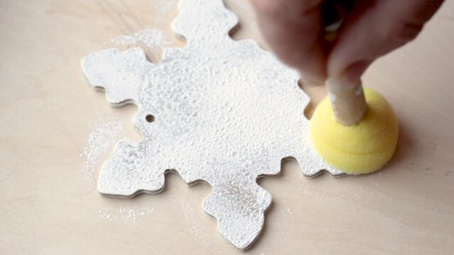 hand woman painting wooden snowflake with yellow sponge brush.fir tree christmas toy homemade.DIY concept,do it yourself.teacher show to studens childrens how to diy object.holiday winter season
