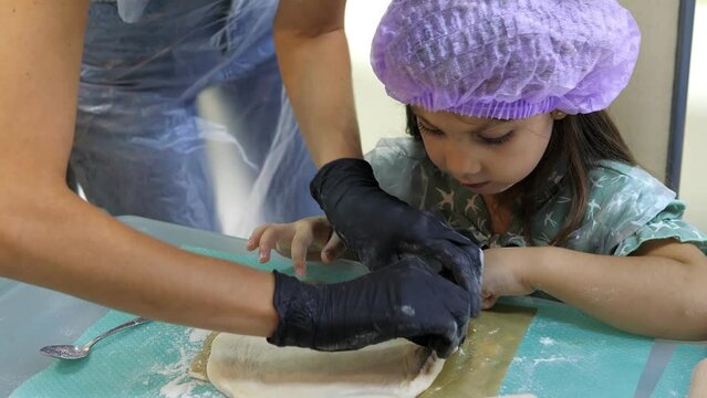 Pretty 5-year old girl in cap making bumpers of raw dough for baking at the master class.Preparing dough for pizza,pie.Stages of baking and confectionery preparation.Children's activity about cooking