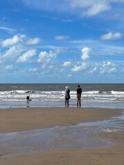 Couple walking there dog on the beach with waves crashing onto the beach. Taken in Fleetwood Lancashire England. 