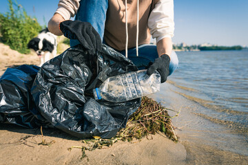 Volunteer sit and picking up garbage on the beach. Cleaner collecting garbage on the sand beach...