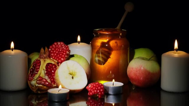Happy Rosh Hashanah concept. Honey, apples and pomegranates ready to eat. Burning candles on black background.