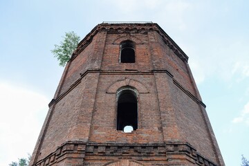 An old brick water tower with arched windows, on the roof of which a tree grows