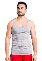 Young handsome man wearing swimwear and sleeveless t-shirt smiling looking to the side and staring away thinking.