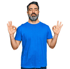 Middle aged man with beard wearing casual blue t shirt relax and smiling with eyes closed doing meditation gesture with fingers. yoga concept.