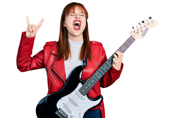 Redhead young woman playing electric guitar doing rock gesture angry and mad screaming frustrated...