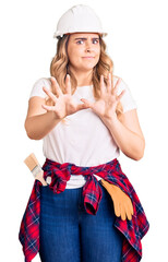 Young caucasian woman wearing security helmet afraid and terrified with fear expression stop gesture with hands, shouting in shock. panic concept.