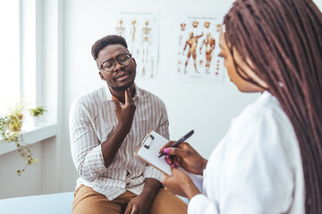 Doctor listens to the patient's complaints while the patient points to the Throat. A doctor listens to a man patient describe throat pain. Young man have problem with sore throat or thyroid gland.