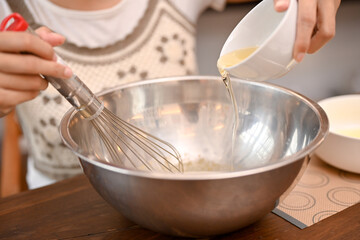Fototapeta na wymiar A female pouring a cup of egg white in the mixing bowl and whisk it together. ccropped image