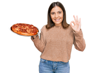 Young beautiful woman holding italian pizza doing ok sign with fingers, smiling friendly gesturing excellent symbol