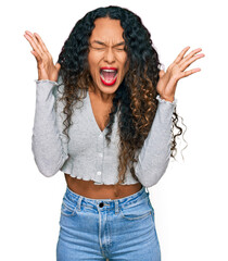 Young hispanic woman with curly hair wearing casual clothes celebrating mad and crazy for success with arms raised and closed eyes screaming excited. winner concept