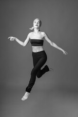 Fototapeta na wymiar Sport, fashion and make-up concept. Slim and beautiful woman with black and tight sport outfit and scarf jumping in air. Graceful pose freeze in motion. Black and white image
