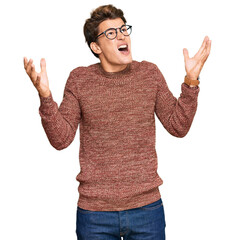 Handsome caucasian man wearing casual sweater and glasses crazy and mad shouting and yelling with aggressive expression and arms raised. frustration concept.