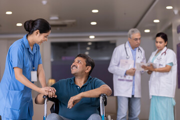 Nurse talking to disabled patient in wheelchair while doctors discussing in background at the...