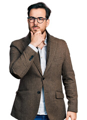 Young hispanic man wearing business jacket and glasses with hand on chin thinking about question,...