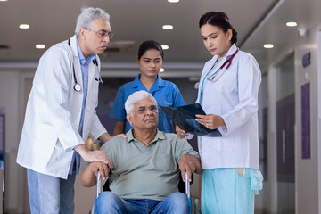 Obraz premium Doctors comforting disabled elderly patient in wheelchair at hospital 
