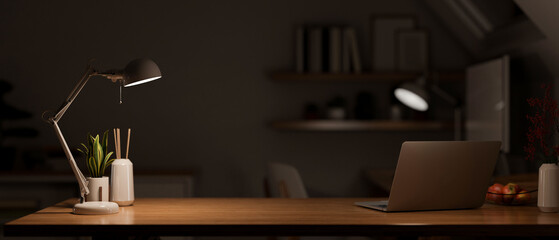 Modern dark wooden office desk at night under the warm light from table lamp with laptop - Powered by Adobe