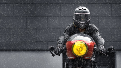 Motorcycle rider in helmet on motorcycle, looking at camera in winter during snowfall