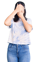 Young beautiful girl wearing casual t shirt covering eyes and mouth with hands, surprised and shocked. hiding emotion