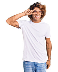 Fototapeta premium Young hispanic man wearing casual white tshirt doing peace symbol with fingers over face, smiling cheerful showing victory