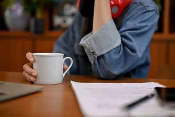 A hipster female in jean jacket at her working desk, holding a mug of coffee. cropped image