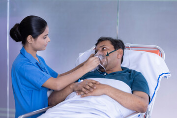 Nurse adjusting a positive pressure oxygen mask on a woman patient lying in bed on a hospital
