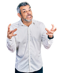 Middle age hispanic with grey hair wearing casual white shirt shouting frustrated with rage, hands trying to strangle, yelling mad