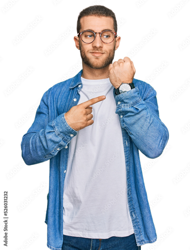 Wall mural Young caucasian man wearing casual clothes in hurry pointing to watch time, impatience, looking at the camera with relaxed expression