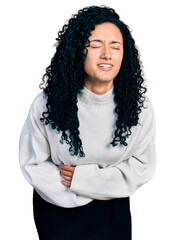 Young hispanic woman with curly hair wearing casual sweater with hand on stomach because nausea, painful disease feeling unwell. ache concept.