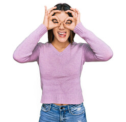 Young hispanic girl wearing casual clothes doing ok gesture like binoculars sticking tongue out, eyes looking through fingers. crazy expression.