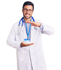 Young hispanic man wearing doctor uniform and stethoscope gesturing with hands showing big and large size sign, measure symbol. smiling looking at the camera. measuring concept.